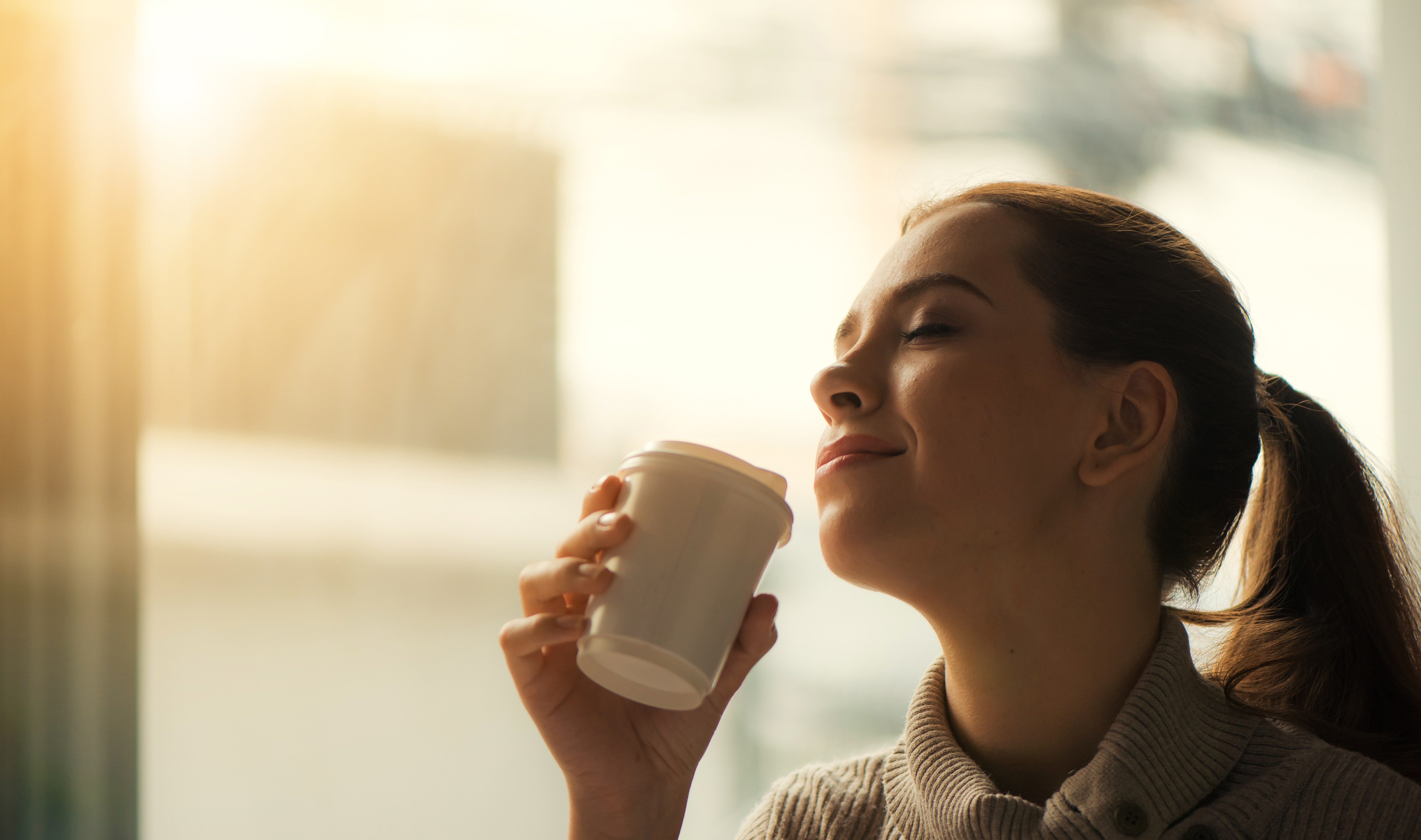 Woman drinking coffee at home with sunrise streaming in through